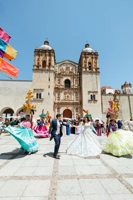Recién casados celebrando con bailarines regionales frente a una catedral histórica en su Destination Wedding urbana.