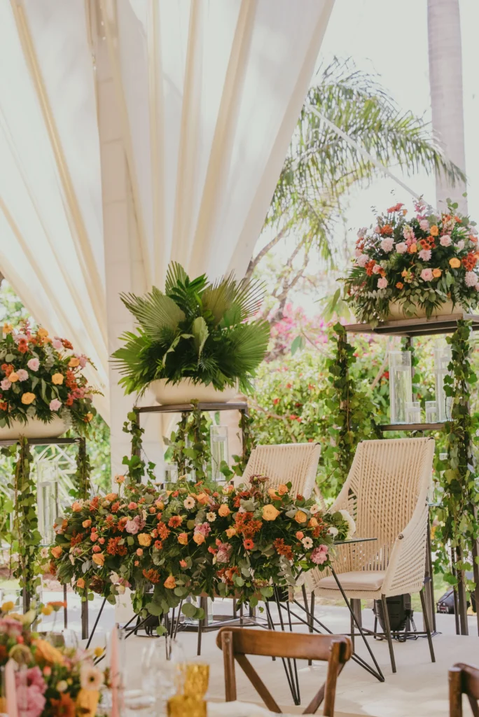 Mesa de honor con abundantes flores en tonos naranja y rosa para una celebración de despedida de soltera al aire libre.