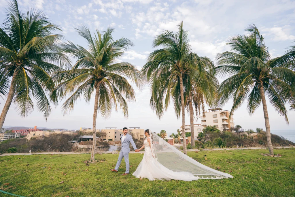 Cómo organizar una boda: Fotografía de una pareja de recién casados caminando por el pasto tomados de la mano.