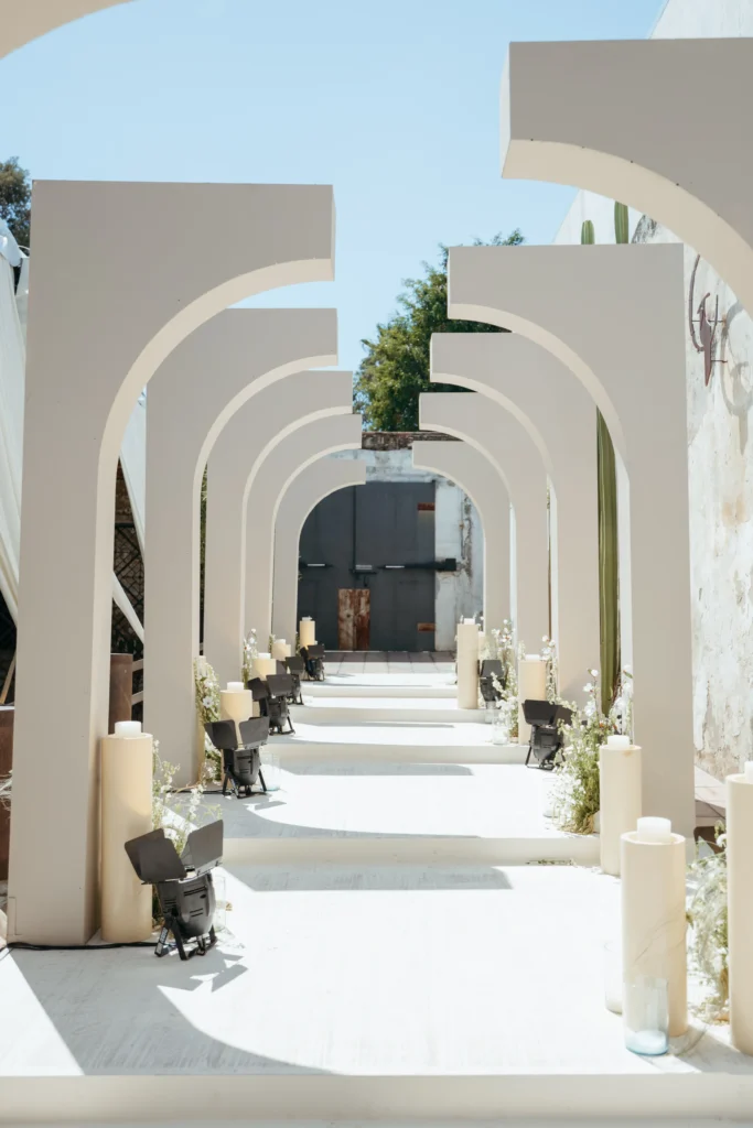 Pasillo con arcos arquitectónicos modernos y velas, ideal para la entrada triunfal en lujosas bodas en la playa.