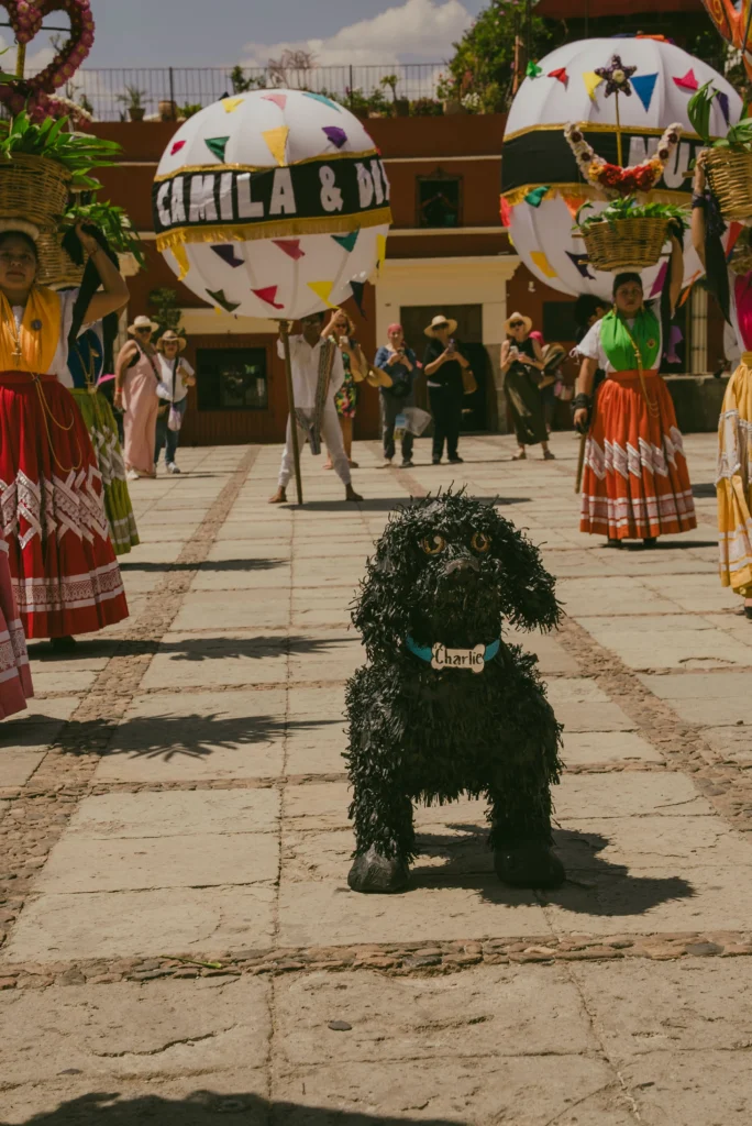 Tradicional calenda oaxaqueña con figuras de papel y un perro "Charlie" celebrando un alegre matrimonio igualitario.